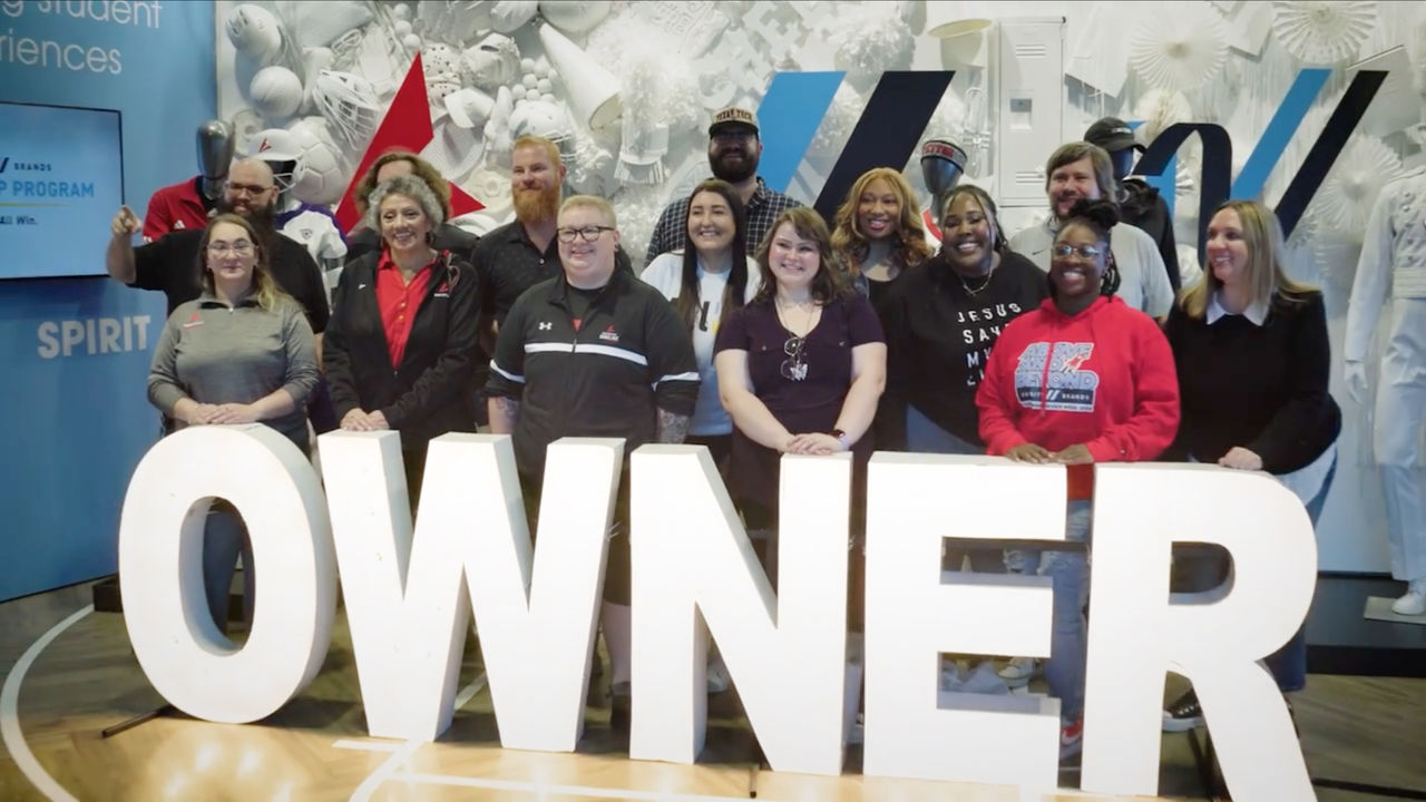 Smiling employees pose for a picture behind a large floor sign that reads "OWNER"